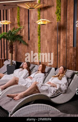Three Caucasian Relaxed Women Having Rest After Spa, Wearing Bathrobes, Lying With Eyes Closed, Boodycare And Healthy Lifestyle Concept Stock Photo