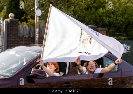 One of the cavalcade of cars passing through Ballymurphy, Eileen McKeown, the daughter of Joseph Corr, sits in the passenger seat with a white flag bearing victim, Joseph Corr's picture and the word 'innocent'. The cars made their way through the streets on Tuesday evening beeping their horns and waving the white flags just hours after a coroner ruled that the 10 people killed in the west Belfast shootings involving British soldiers in Ballymurphy in August 1971 were entirely innocent. Picture date: Tuesday May 11, 2021. Stock Photo