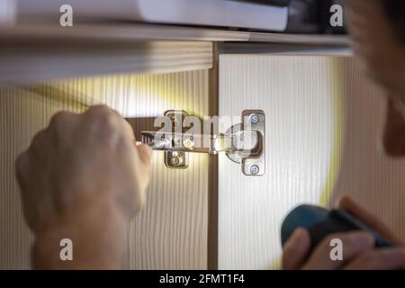 An unrecognizable man installs a door on a wardrobe, fixes furniture with a screwdriver. Only hands are visible. Close-up. Renovation concept, furnitu Stock Photo