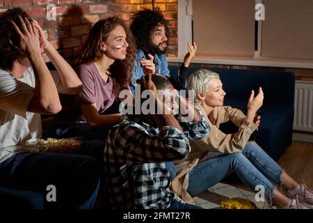 upset friends supporting football team at home, cheering for favourite team, feel concern. sit on sofa at home, in dark room at night Stock Photo