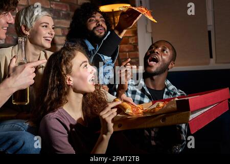 happy friends eating pizza and watching movie or tv series at home, american students enjoy spare free time after lessons, having rest after hard week Stock Photo