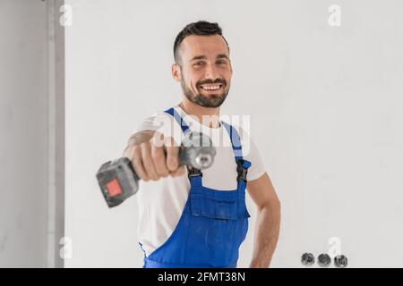 A young repairer holds a drill in his hand. He smiles and looks at the camera Stock Photo