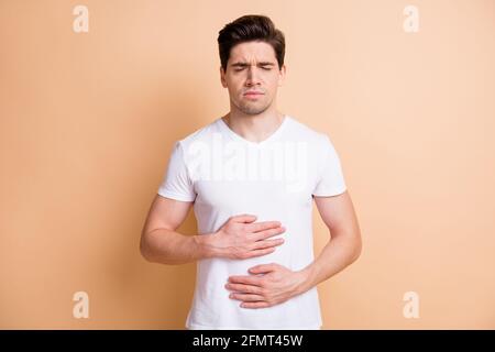 Photo of young man closed eyes holding hands on belly feels bad isolated on beige color background Stock Photo