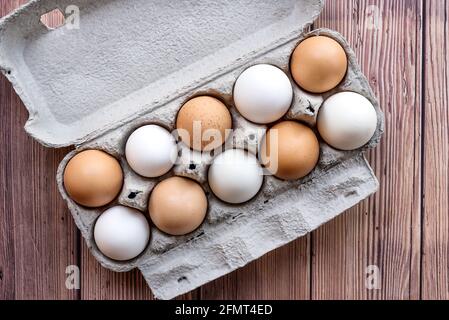 A cardboard egg box with ten brown and white eggs on a wooden table. Mixed eggs in a box - Top View Stock Photo