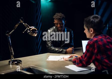 A beautiful tattooed feminist girl gives advice to a black man on choosing an individual sketch of a tattoo on his face Stock Photo