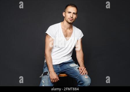 A cheerful young guy in a white blank t-shirt and jeans posing over black background. A handsome adult man in a casual outfit posing in the dark Stock Photo