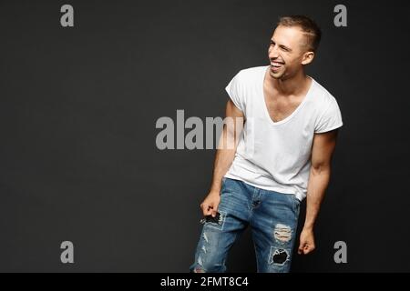 A cheerful young guy in a white blank t-shirt and jeans posing over black background. A handsome adult man in a casual outfit posing in the dark Stock Photo
