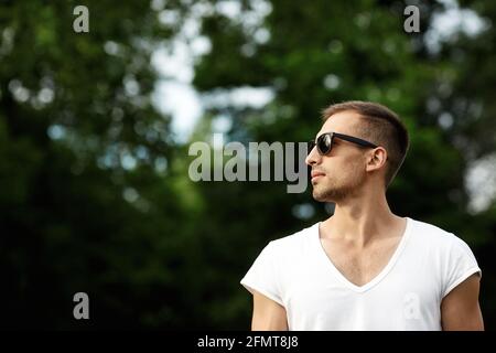A handsome young man posing outdoors in black sunglasses and a casual outfit. Stock Photo
