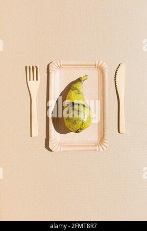 Pear wrapped in polyethylene plastic on the beige paper background. Immature, tasteless or inedible food concept. Vertical photo. Copy space. Flat lay Stock Photo