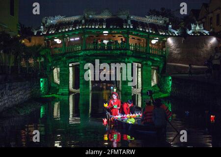 Vietnamese couple sat in boat in front of Japanese Bridge release colourful floating lanterns into river, Hoi An, Vietnam Stock Photo