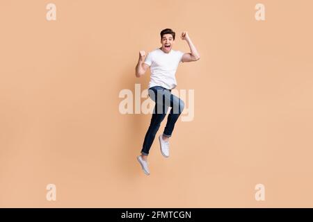 Full size profile photo of hooray brunet man jump wear t-shirt jeans sneakers isolated on beige background Stock Photo