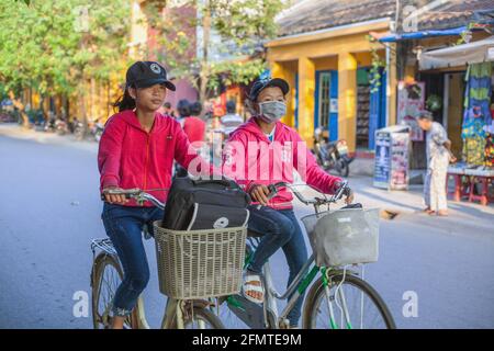 Vietnamese schoolgirls ride side by side on their bicycles through old town Hoi An, Vietnam Stock Photo