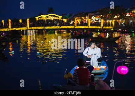 Vietnamese couple kissing sat in boat release colourful floating lanterns into river, Hoi An, Vietnam Stock Photo
