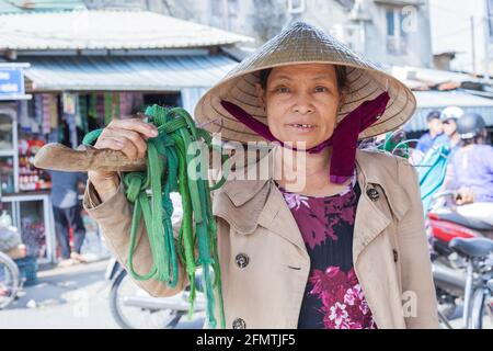 Close up portrait of Vietnamese female wearing conical hat carrying shoulder pole, Hoi An, Vietnam Stock Photo