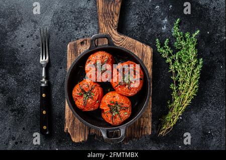 Roasted cherry tomatoes with thyme in a pan. Black background. Top view Stock Photo