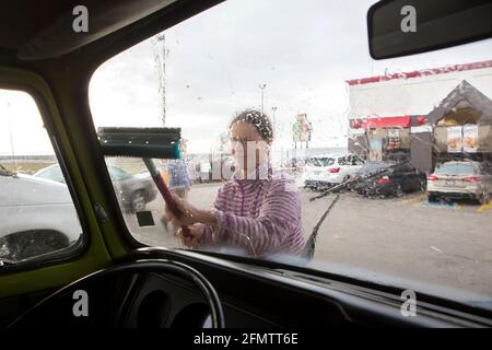 A woman cleans the windshield of VW camper van during roadtrip Stock Photo