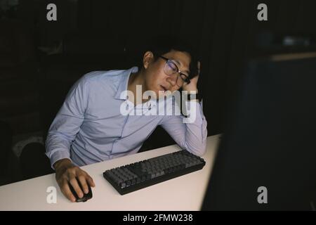Young Asian businessman working overworked in corporate office. Male office worker sleepy during overtime hours at night Stock Photo
