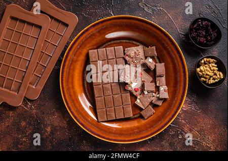 Homemade milk chocolate with hazelnuts, peanuts, cranberries and freeze dried raspberries on a rustic plate. Dark background. Top view Stock Photo