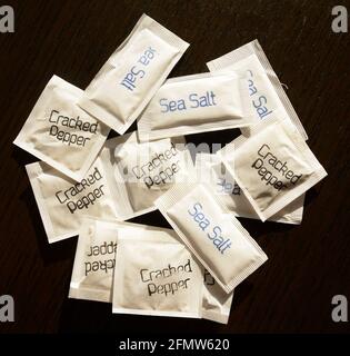 individual sachets of salt and pepper on a dark wooden table Stock Photo