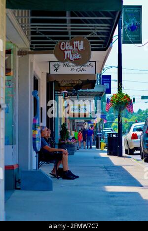 Mount Airy, North Carolina, USA - July 5, 2020: A couple relax on a bench in the shade in historic downtown Mount Airy on a hot summer afternoon. Stock Photo