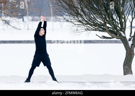 Young man doing makes stretching in morning exercises, doing fitness outdoors in winter. Stock Photo