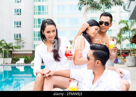 Asian couples sitting by hotel swimming pool Stock Photo - Alamy