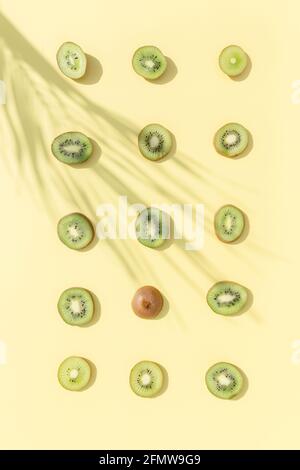Slices and cuts of kiwi fruit pattern on yellow background. Healthy eating, travel or vacation concept Stock Photo