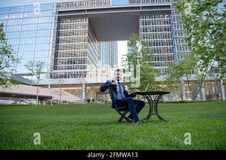 Businessman typing on laptop computer sitting at table on office terrace. Man working remotely in modern park. Stock Photo