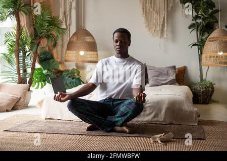 Young african man meditating sitting at his bedroom in the morning Stock Photo
