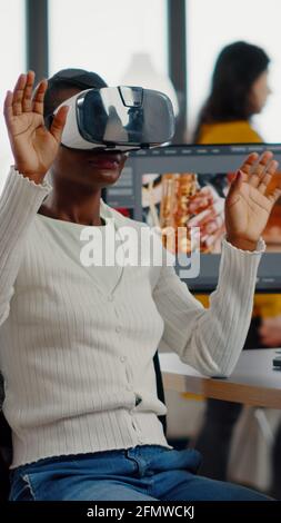 African video editor experiencing VR goggles, gesturing, editing video film montage working with footage and sound on computer with two displays. Videographer processing movie in creative agency Stock Photo