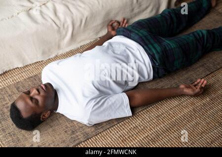 Young black man lying in Dead Body exercise or Corpse pose with his eyes closed, Savasana pose Stock Photo