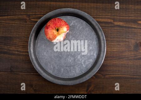 Bitten apple on a metal plate. Dark wood texture table. Stock Photo