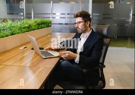 Young business man in office work online on laptop solve business problem. Pensive businessman use computer thinking pondering over project.  Stock Photo