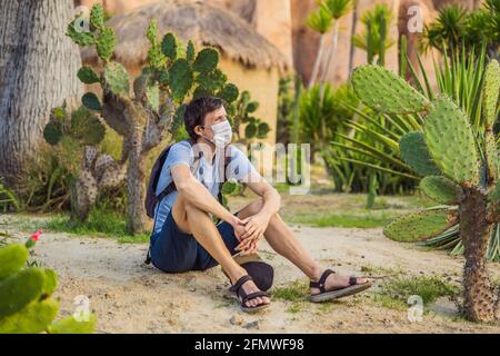 beautiful stylish young man in desert among the cacti, wearing a medical mask during COVID-19 coronavirus, traveling in Africa on safari, exploring Stock Photo