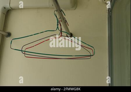 Closeup damaged steel clothes hangers covered with plastic hanging on clothesline at the balcony, selective focus on the green one Stock Photo