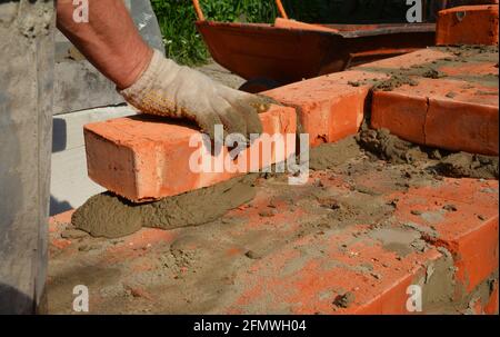 A mason person is laying a brick wall or foundation of a new house. A close-up of a brickwork when a builder is laying a course of bricks on mortar. Stock Photo