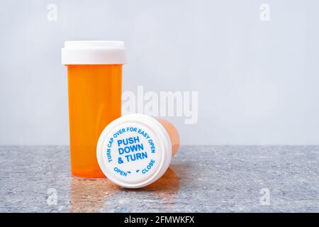 Two orange prescription bottles with safety caps on glossy gray surface on white background, one bottle standing, other lying Stock Photo