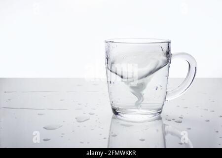 https://l450v.alamy.com/450v/2fmwkkr/transparent-glass-mug-with-water-on-light-surface-with-water-drops-water-in-the-form-of-tornado-inside-mug-soft-focus-a-storm-in-a-teacup-2fmwkkr.jpg