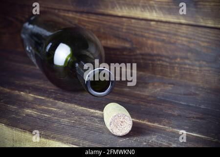 Lying empty wine bottle with cork nearby on plank wooden surface. Stock Photo