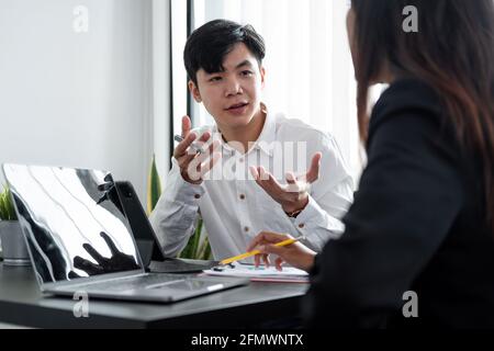 Young asian male mentor coach worker talking to female coworker teaching intern having business conversation with workmate, serious hindu manager Stock Photo