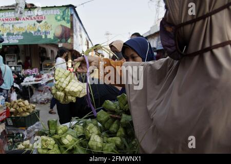 West Java, Indonesia. 12th May, 2021. A woman buys 'Ketupat' in Bekasi, West Java, Indonesia, on May 12, 2021. 'Ketupat', a traditional rice cake boiled in plaited coconut leaves, is often sold prior to Eid al-Fitr festival. Credit: Aditya Irawan/Xinhua/Alamy Live News Stock Photo