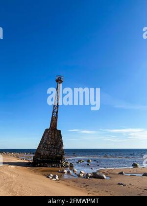 Beautiful sea beach with dune sand and an old abandoned lighthouse. The lighthouse is based on large stones. Stock Photo