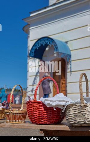 Wicker baskets with eggs and cakes stand on a bench in front of the church on the feast of Bright Easter. Stock Photo