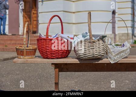 Wicker baskets with eggs and cakes stand on a bench in front of the church on the feast of Bright Easter. Stock Photo
