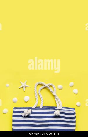 Beach striped bag and white seashells on a yellow background. View from above, flat lay. Space for text. Summer holiday with beach outfit and accessor Stock Photo