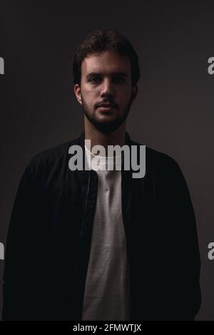 Vertical shot of a bearded Caucasian man with minimalist clothing against a black background Stock Photo