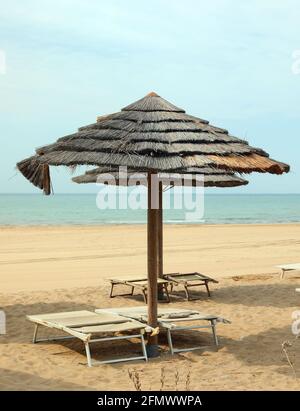 large bamboo sun umbrella on the seashore without people and empty deck chairs Stock Photo