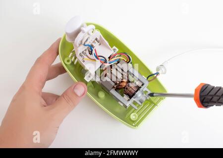 The hands of a male household appliance repairman unscrew the parts of a hand mixer with a screwdriver. Household appliance repair service concept, cl Stock Photo