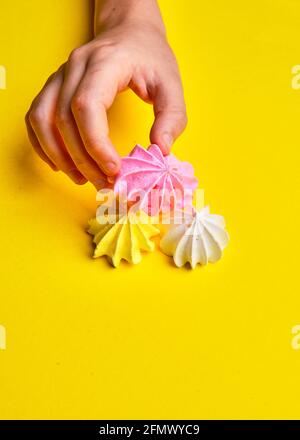 pink meringue in hand on bright yellow background Stock Photo