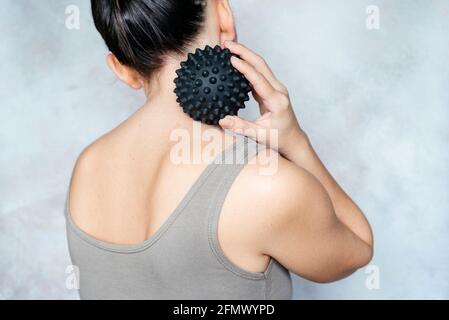 Young woman massages her back with spiky trigger point ball, muscle pain treatment reflexology, deep tissue massage Stock Photo